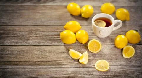 Cup of black tea with lemon slice and plenty of lemons around on wooden table Stock Photos