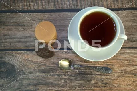 A cup of black tea on a porcelain saucer, a spoon and a stack of sponge cooki Stock Photos