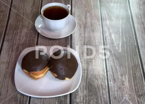 A cup of black tea on a saucer and a plate with two donuts in chocolate icing Stock Photos