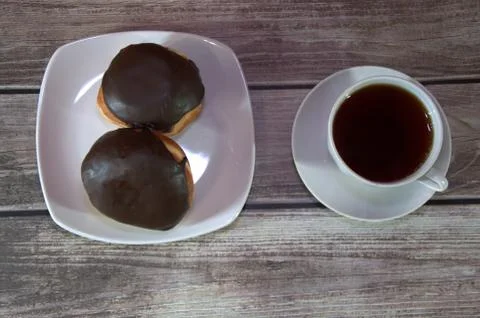 A cup of black tea on a saucer and a plate with two donuts in chocolate icing Stock Photos