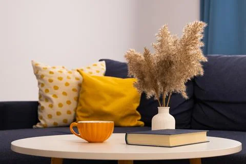A cup with a book on the table against the background of pillows. Home comfort Stock Photos