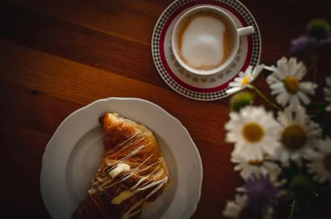 Cup of cappuccino and brioche on a wooden table with fresh flowers Stock Photos