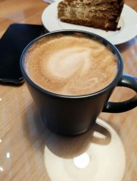 A cup of cappuccino coffee on a table in a cafe next to you can see a plate w Stock Photos