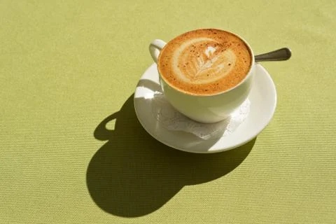 A Cup of cappuccino with a pattern on the table lit by the morning sun. Stock Photos