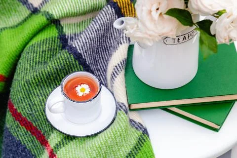 Cup of chamomile herbal tea with chamomile flower and teapot, books, warm pla Stock Photos