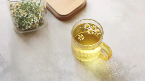 A cup of Chamomile tea on light wooden table with flowers in glass container Stock Footage 246324853