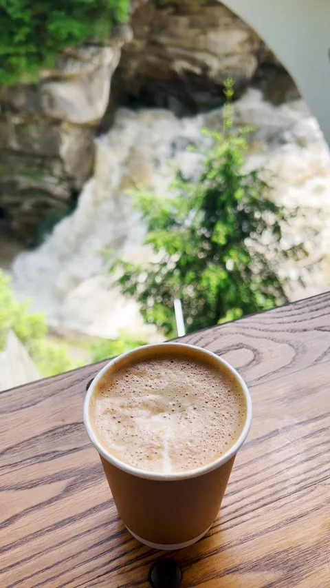 A cup of coffee against the backdrop of a rapid flow of water from a waterfall. Stock Footage 278923742