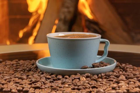 A cup of coffee and coffee beans on a background of burning fireplace. Stock Photos