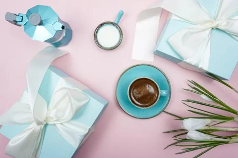 A cup of coffee and a gift box with a white bow on a pink background. Stock Photos