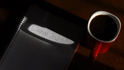 Cup of coffee and a notebook that says damn 2020 Stock Footage 139650253