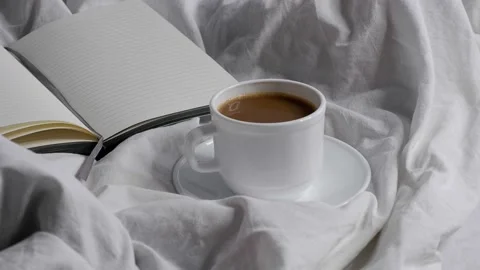 A cup of coffee and a notebook on a white bed. 4k Stock Footage 158295172