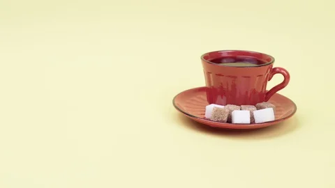 A Cup of coffee and sugar cubes on a yellow background. Stockbeeldmateriaal 129045233