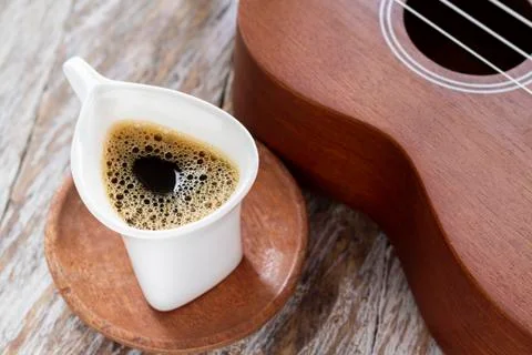 Cup of coffee and ukulele on rustic wood. Stock Photos