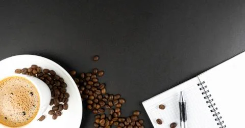 Cup of coffee, aromatic coffee beans on a black background. Notebook and pen Stock Photos