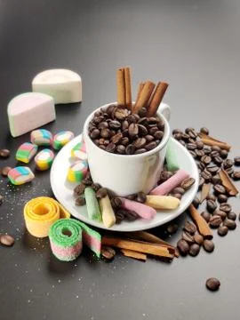 Cup with coffee beans and colored sweets on a black background Stock Photos