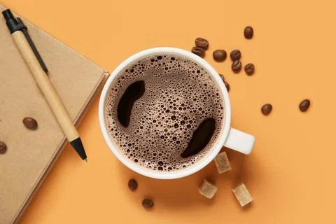 Cup of coffee with beans, notebook and sugar cubes on orange background Stock Photos