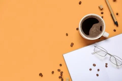 Cup of coffee with beans, notebook, sugar cubes and eyeglasses on orange back Stock Photos