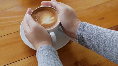 Cup of coffee being held by hands. Person drinking latte art coffee. Stock Footage 334648824