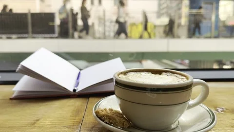 Cup of coffee with a biscuit and an open notebook on a wooden table by a window Stock Footage 297717231