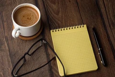 Cup of coffee, blank notepad, pen and glasses on wooden table Foto stock