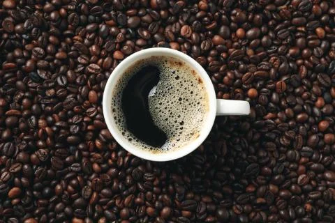 Cup of coffee on coffee beans background, top view Stockfoto's