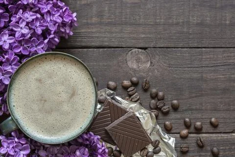 Cup of coffee with coffee beans, chocolate and lilac flowers Stock Photos
