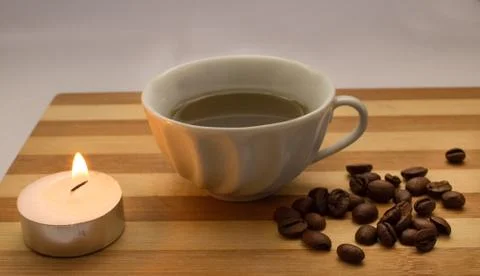A cup of coffee, coffee beans, a lighted candle Stock Photos