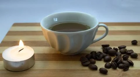 A cup of coffee, coffee beans, a lighted candle Stock Photos