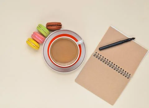 Cup of coffee, colored macaroons, notepad with pen on background.. 写真素材