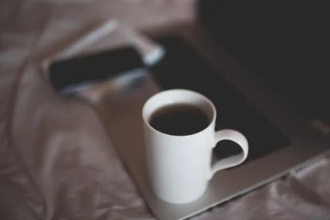 Cup of coffee on computer with phone in bed closeup. Stay at home. Quarantine Stock-Fotos