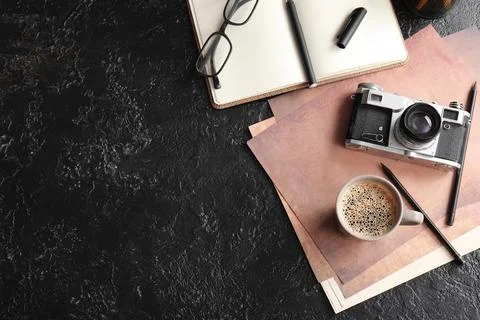 Cup of coffee with documents, camera and eyeglasses on black grunge backgroun Stock-Fotos