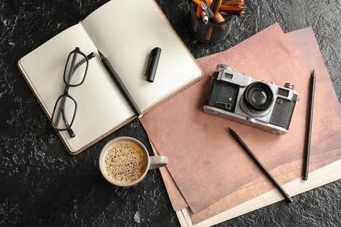 Cup of coffee with documents, camera and eyeglasses on black grunge backgroun Stock Photos