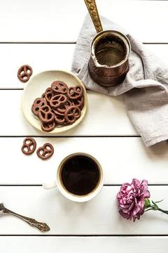 A cup of coffee, empty coffee pot, chocolate-covered pretzels and a flower Stock-Fotos