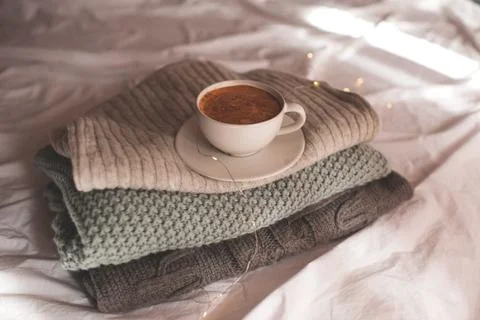 Cup of coffee with foam staying on stack of knitted sweaters close up. Good m Stock-Fotos