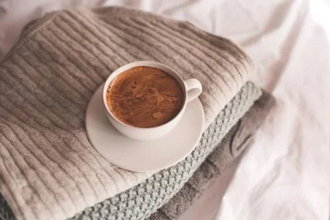 Cup of coffee with foam staying on stack of knitted sweaters close up. Good m Stock-Fotos