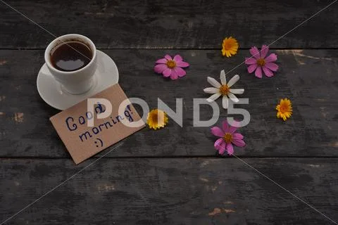 Cup of coffee with good morning sign and flowers on the table Stock Photos