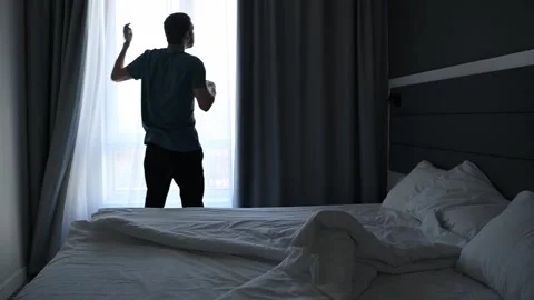 With a cup of coffee in hand, a man opens the curtains and gazes out the window. Stock Footage 307666652