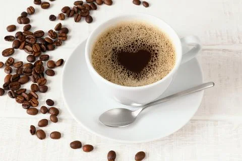 Cup of coffee with heart pattern and coffee beans on white wooden table Top view Stock Photos