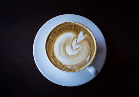 A cup of coffee with heart pattern in a white cup on the dark wooden background Stock Photos