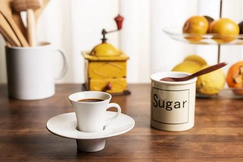 Cup of coffee on a kitchen table with a fruit bowl, a jug with wooden utens.. Stock Photos