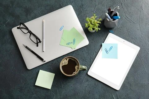 Cup of coffee with laptop, tablet computer and eyeglasses on green grunge bac Stock Photos