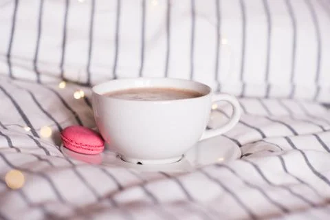 Cup of coffee with macaron cookie in bed with lighs. Stock Photos
