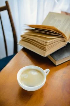 A Cup of coffee with milk on a wooden table with an open book in the background Stock Photos