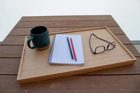 A cup of coffee, notebook, and glasses rest on a wooden tray. Stock Photos