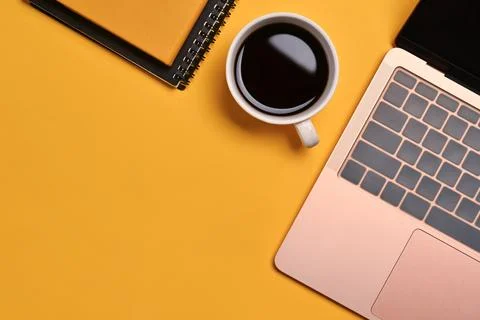 A cup of coffee, notebook and laptop on yellow background. Top view with copy Foto stock