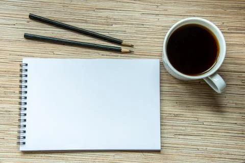A cup of coffee, notebook with two pencils on wooden background. Cosy workspa Stock Photos