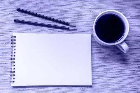 A cup of coffee, notebook with two pencils on wooden background. Cosy workspa Stock Photos