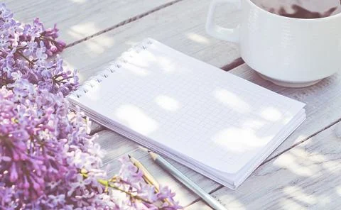 Cup of coffee, notepad, and a lilac branch on the white wooden table Stock-Fotos