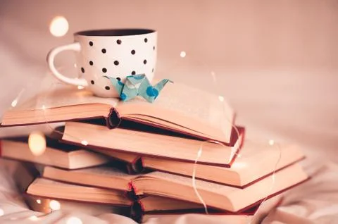Cup of coffee with origami crane on stack of open books close up. Good mornin Stock Photos
