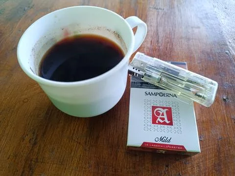 A cup of coffee, a pack of Sampoerna Mild cigarettes and a lighter on the table. Stock Photos